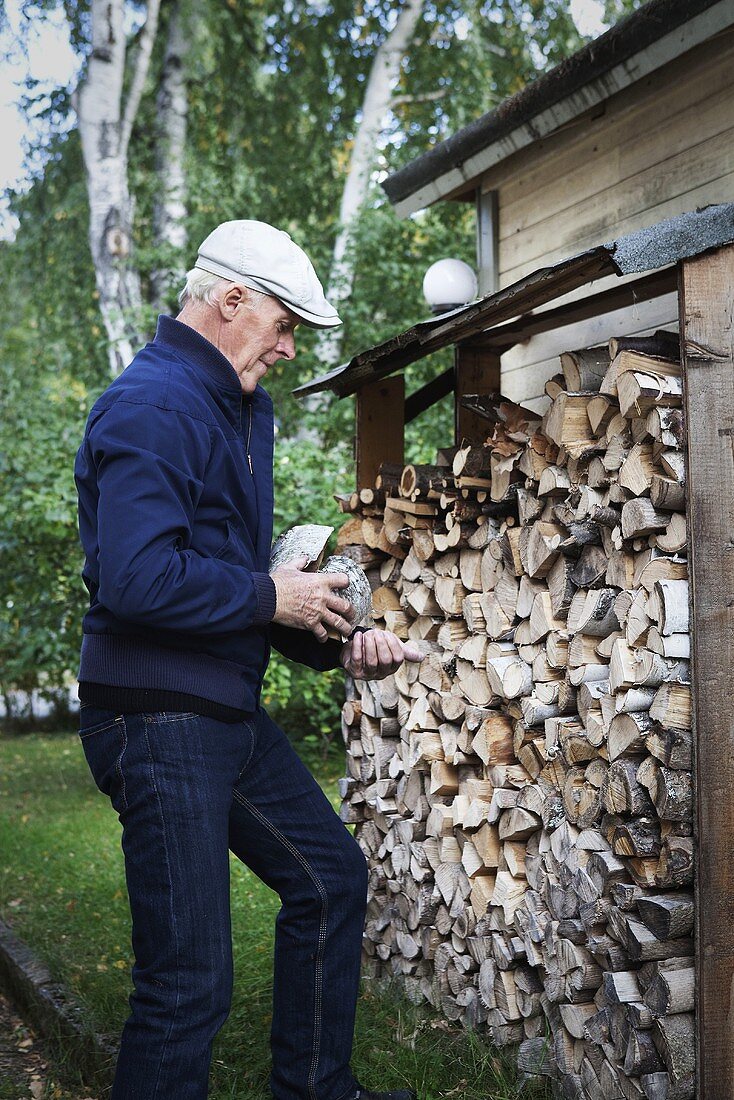 Älterer Mann mit Holzscheiten am Kaminholzunterstand