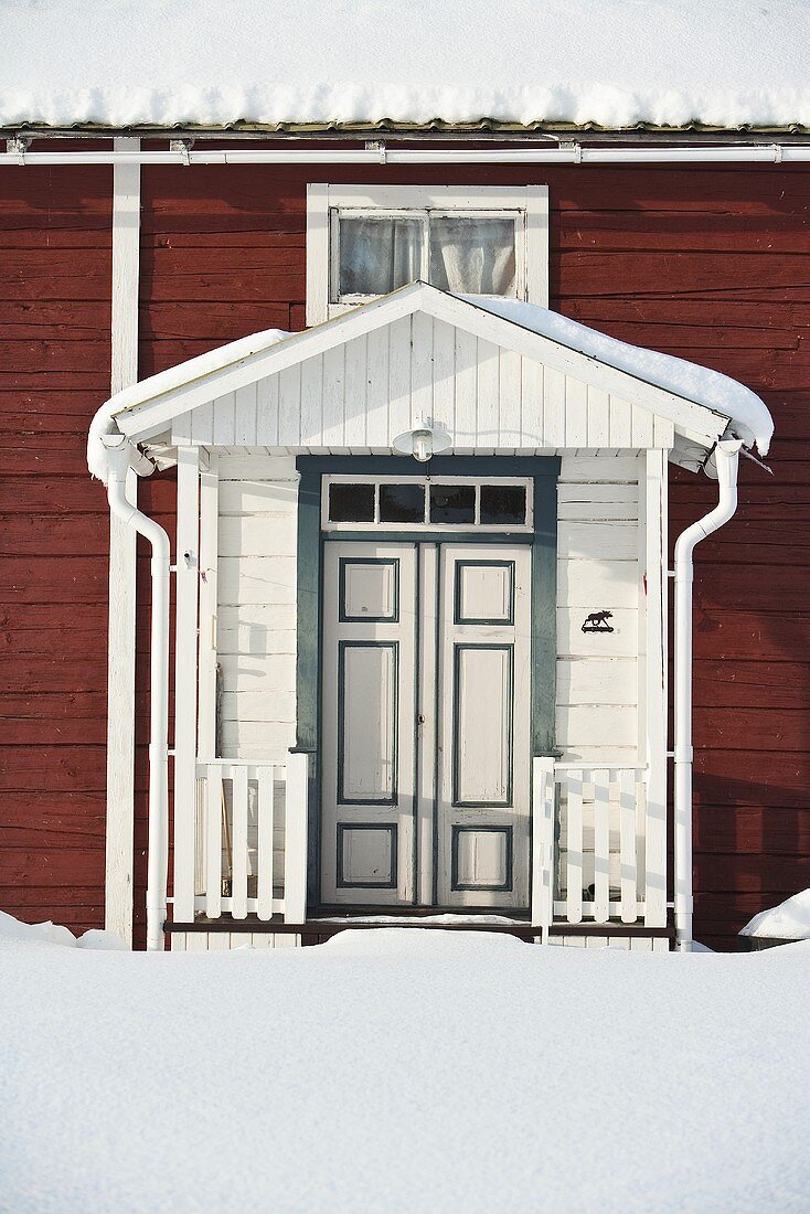 weiße überdachte Eingangstür eines braunen Holzhauses im Winter