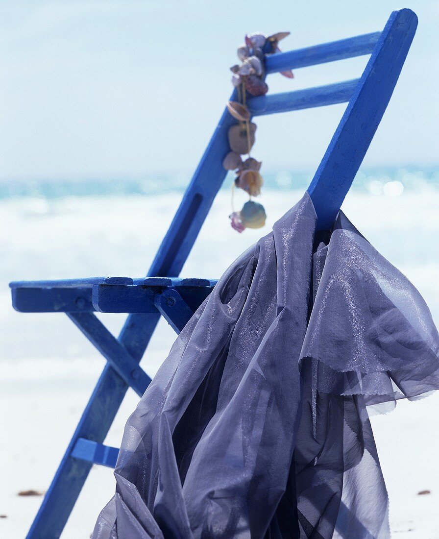 Holzstuhl, dekoriert mit Muscheln und blauem Tuch, am Meer