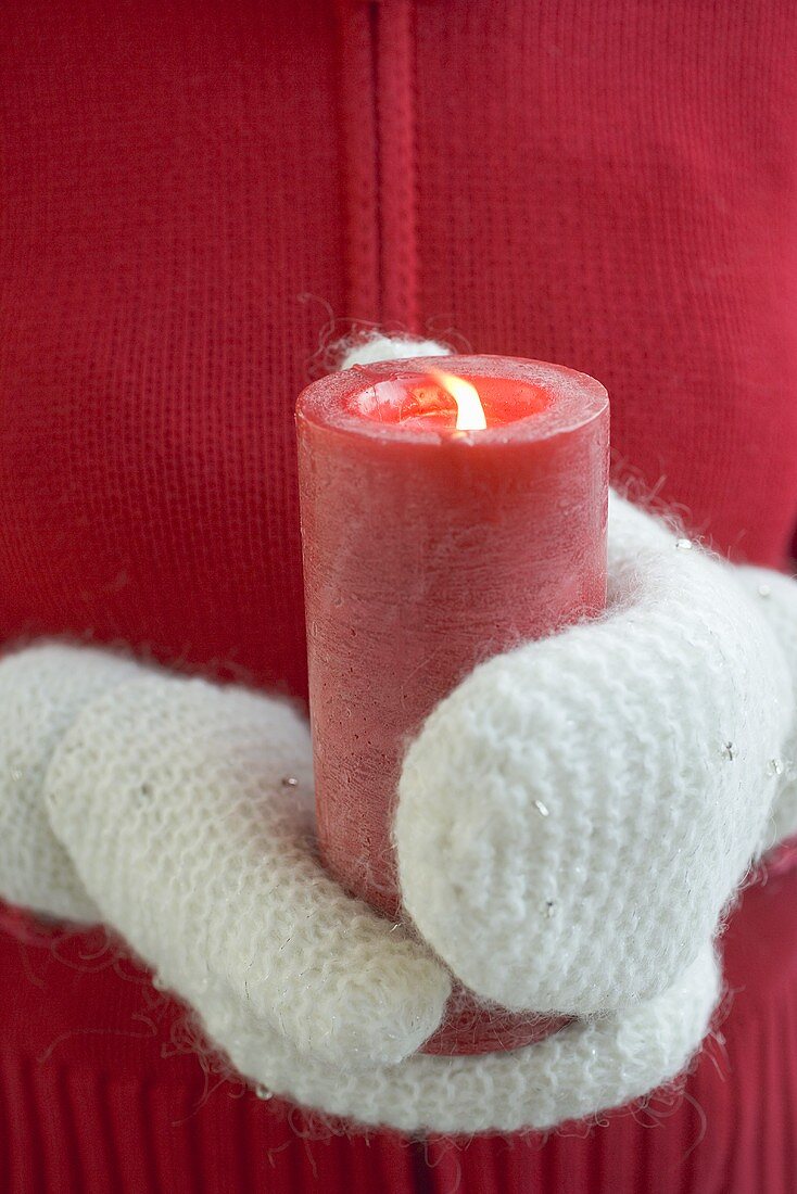 Hands in mittens holding burning candle