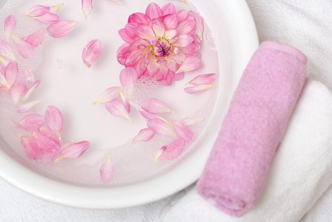 Rosa Blütenblätter in Wasserschale, daneben Handtücher