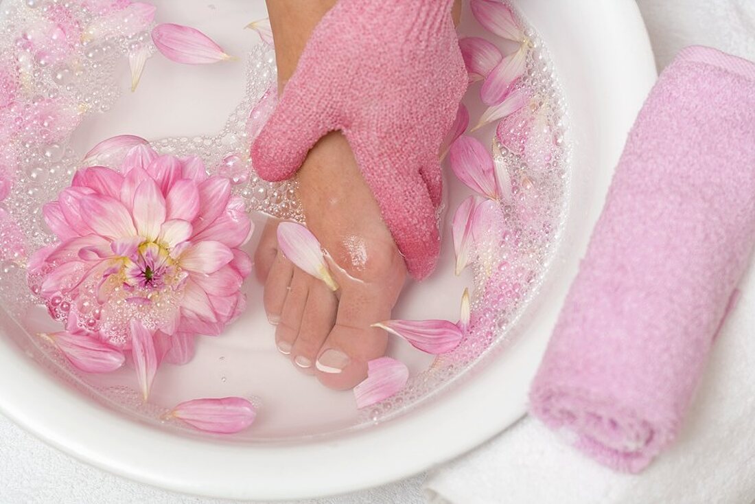 Frau wäscht ihren Fuss mit rosa Peelinghandschuh