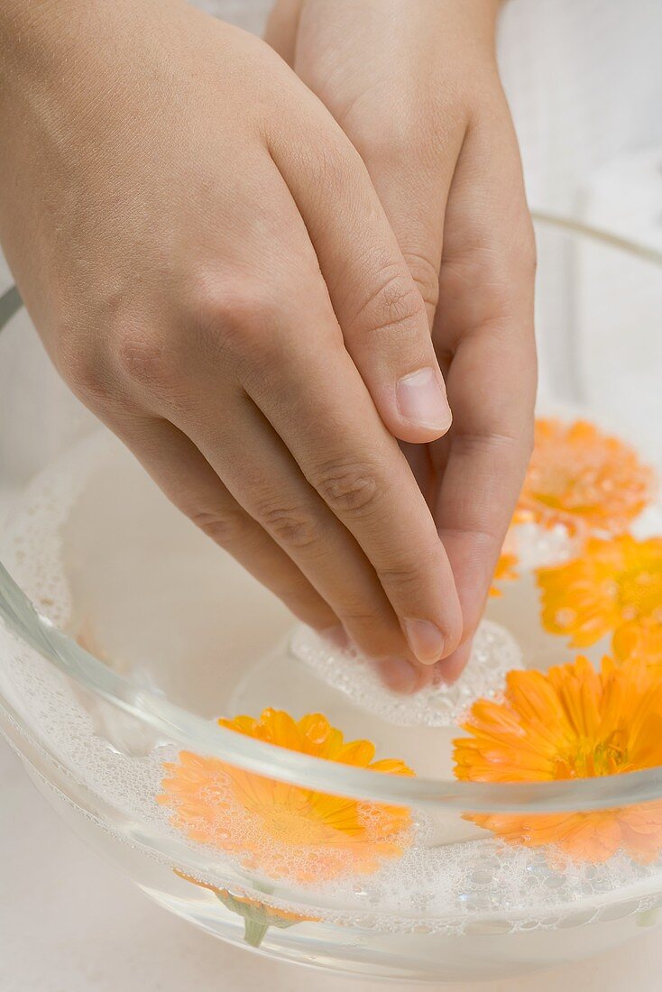 Frau taucht ihre Hände in Seifenwasser mit Ringelblumen