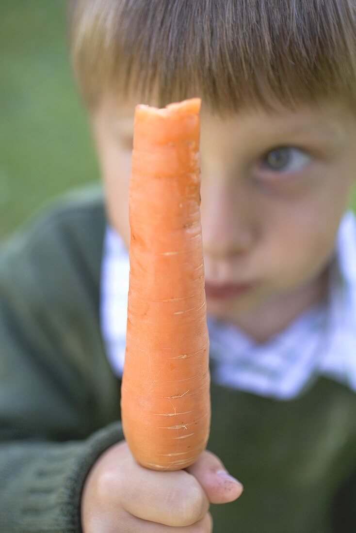 Boy holding a partly-eaten carrot