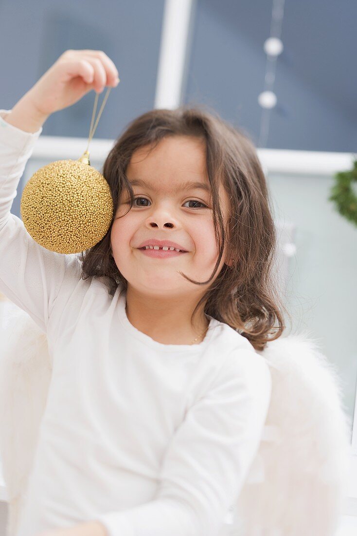 Kleines Mädchen hält goldene Christbaumkugel