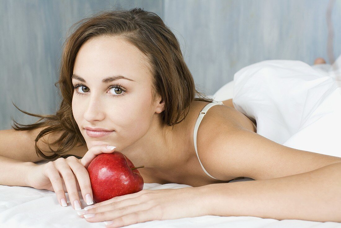 Young woman with a red apple in bed