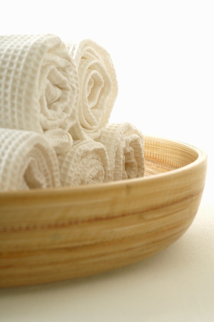 Rolled white towels in a wooden bowl