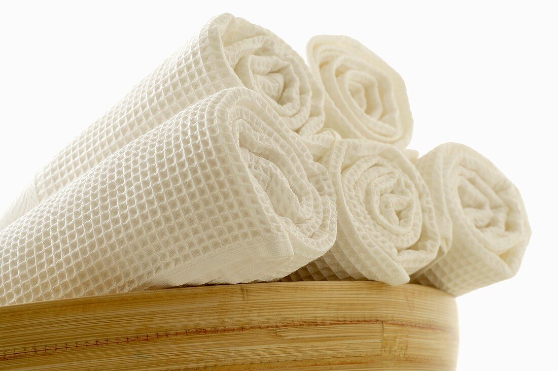 Rolled white towels in a wooden bowl