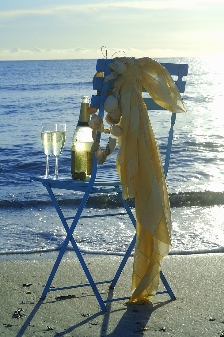 Two glasses of sparkling wine with bottle on chair by sea
