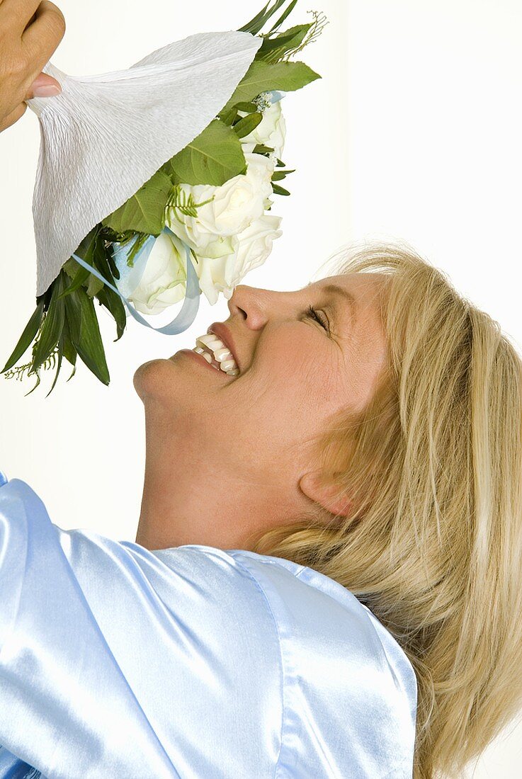 Lächelnde Frau riecht an Strauss mit weissen Rosen