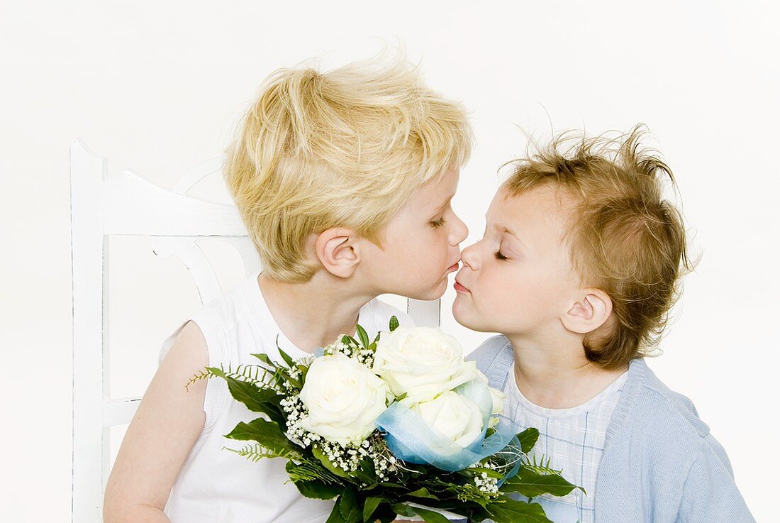 Zwei küssende Kinder halten weissen Rosenstrauss