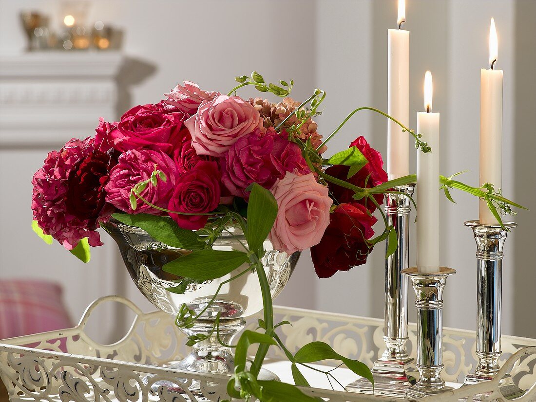 Red flower arrangement in silver bowl, candles beside it