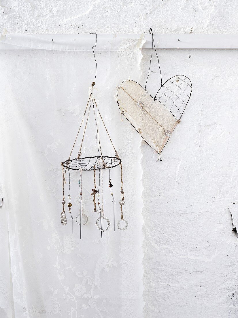 Two wind chimes (one heart-shaped) hanging on a white wall