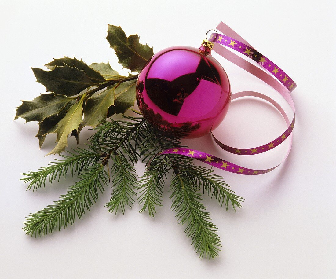 Pink Christmas bauble with sprigs of fir and holly