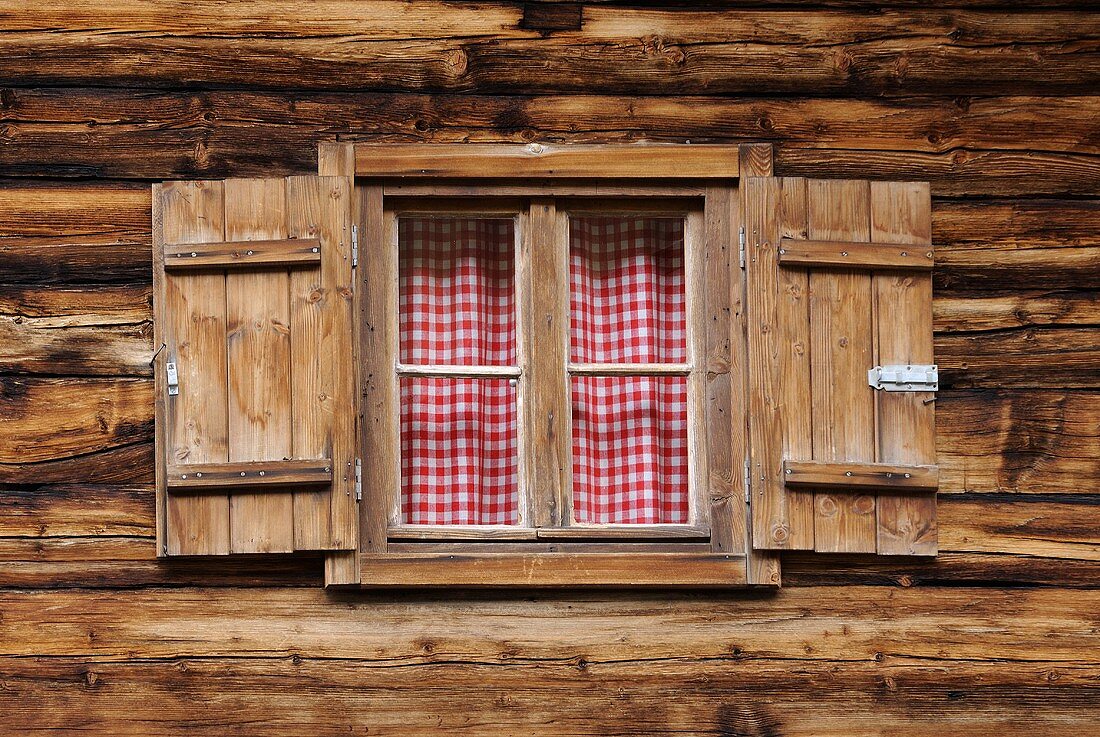 Fenster einer rustikalen Holzhütte mit weiss-rot karierten Vorhängen