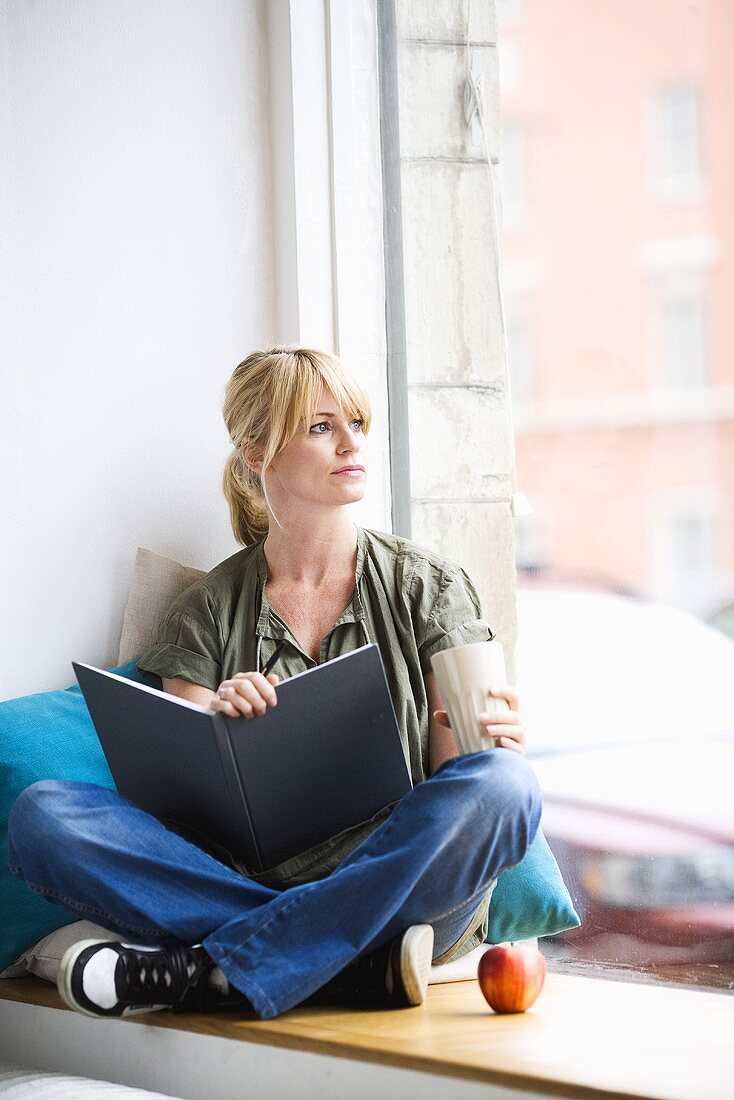 Blond woman sitting by window with a book