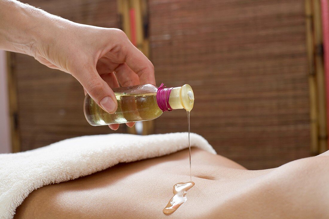 Masseur pouring massage oil on woman's stomach