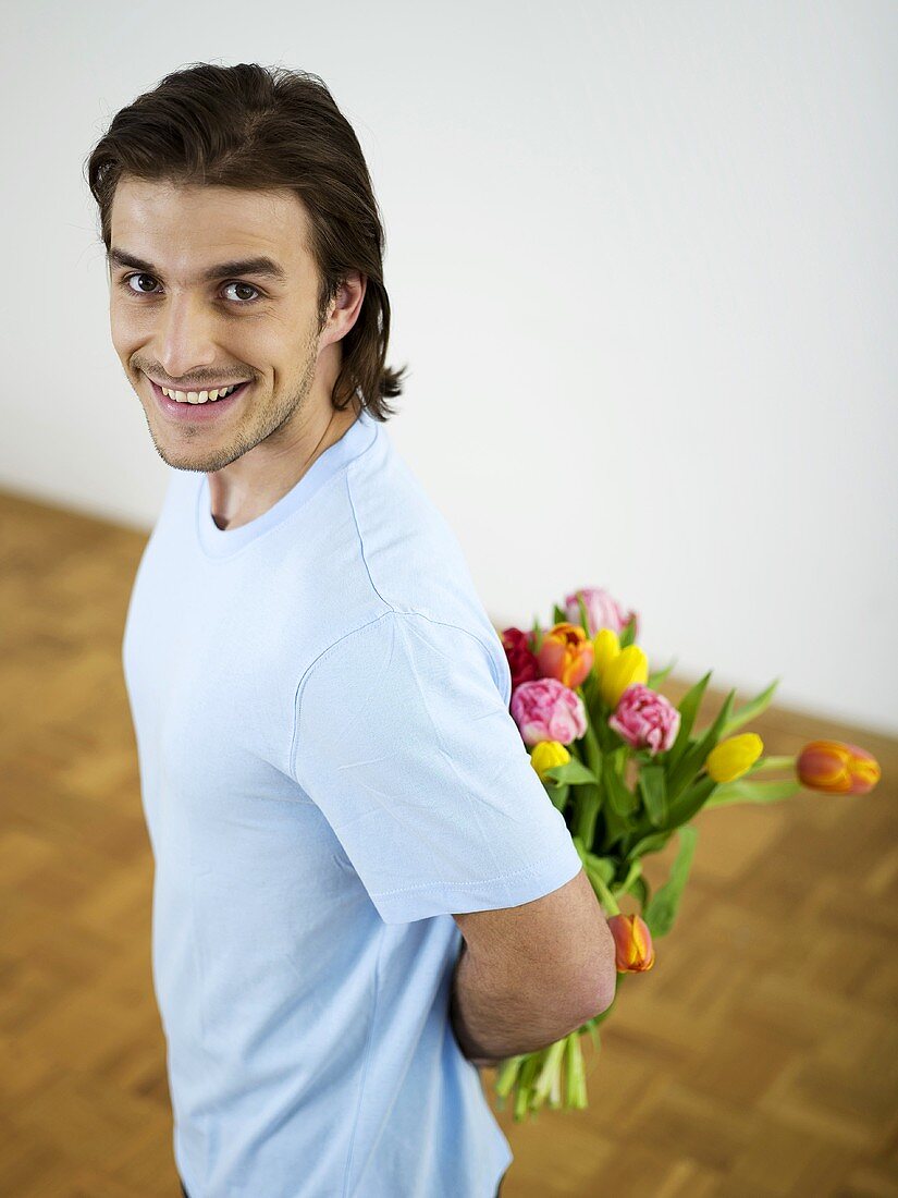 Junger Mann mit Blumenstrauss hinter dem Rücken