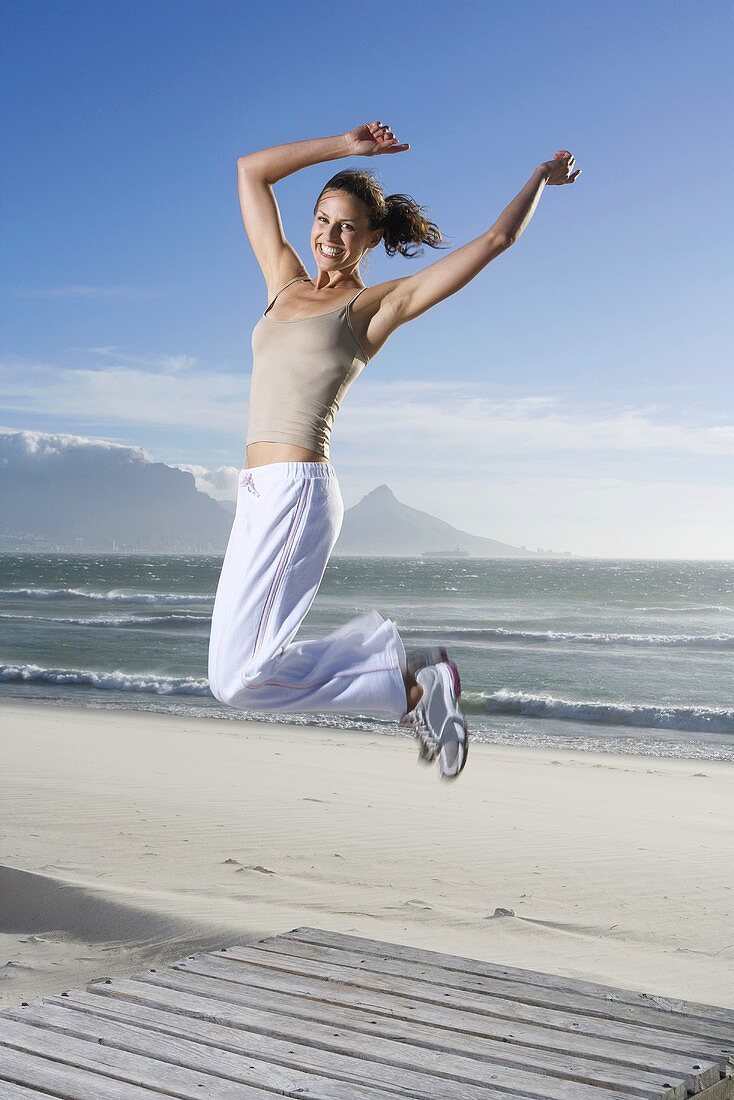 Frau macht Luftsprung am Strand (Südafrika)