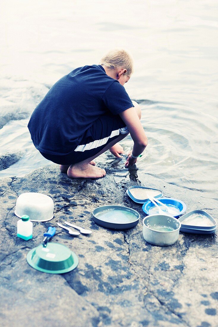 Boy rinsing dishes in river