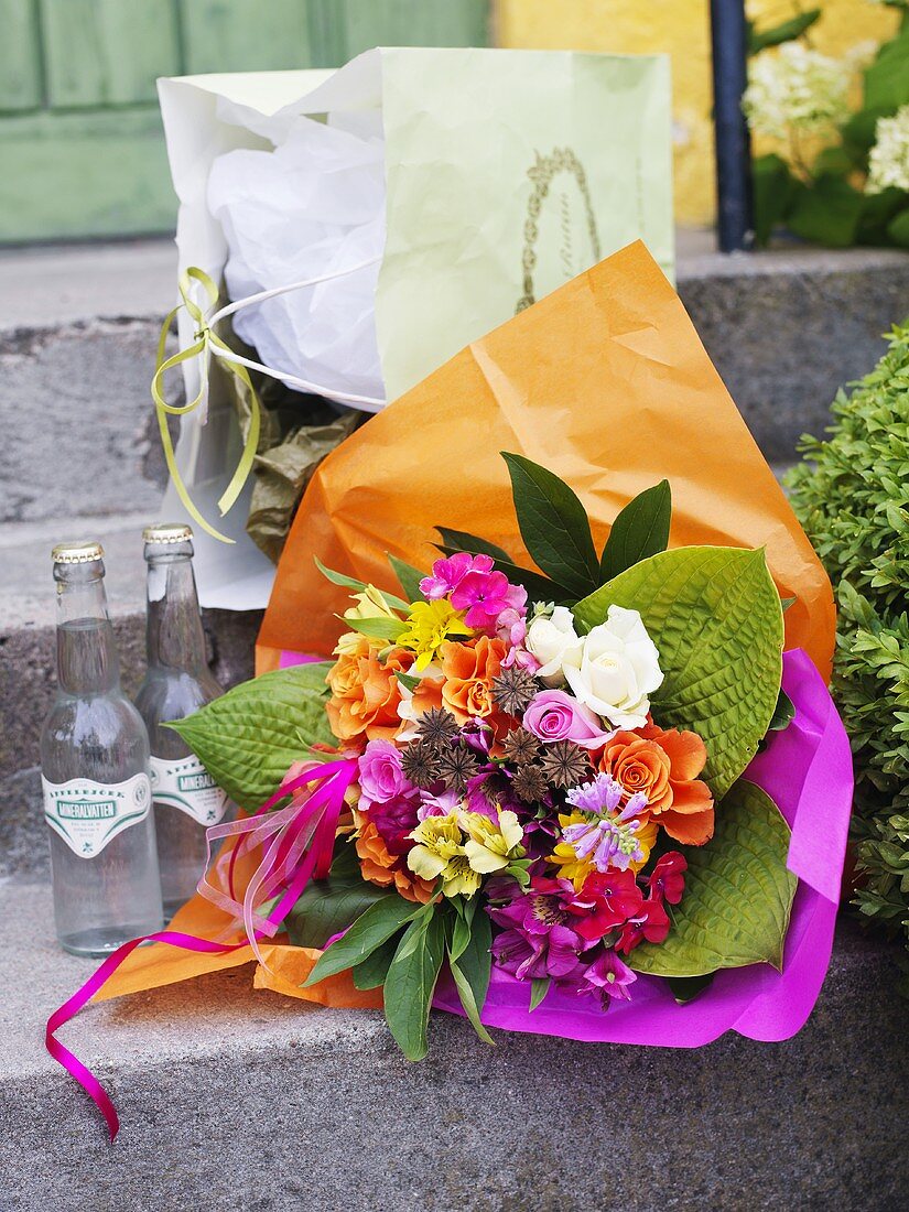 Sommerlicher Blumenstrauss, Getränkeflaschen und Einkaufstüte vor Haustür