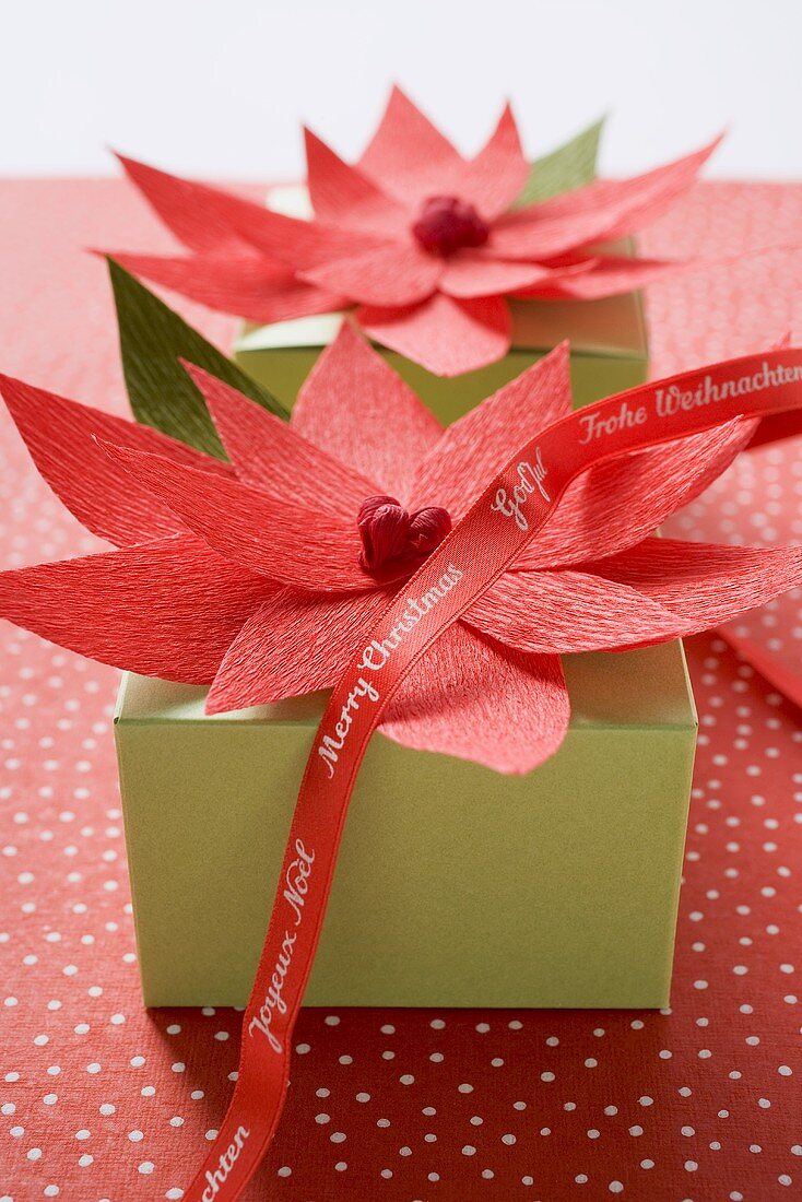 Zwei Weihnachtspäckchen, dekoriert mit roten Papierblüten
