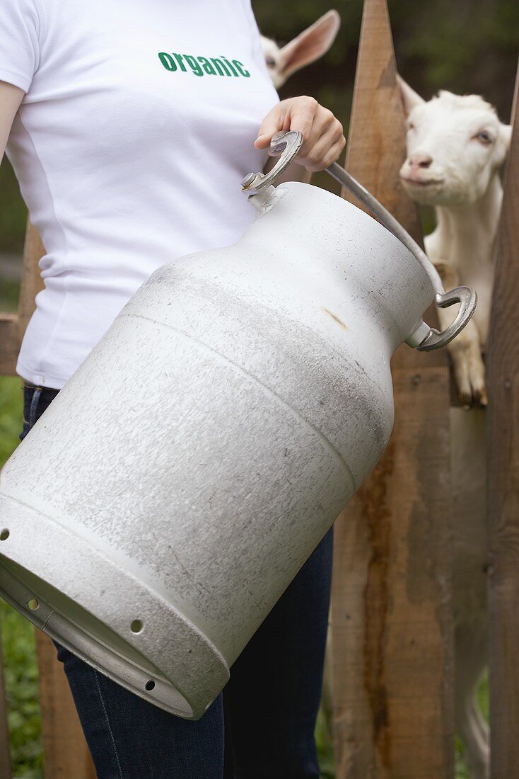 Frau mit Milchkanne vor einem Ziegenstall