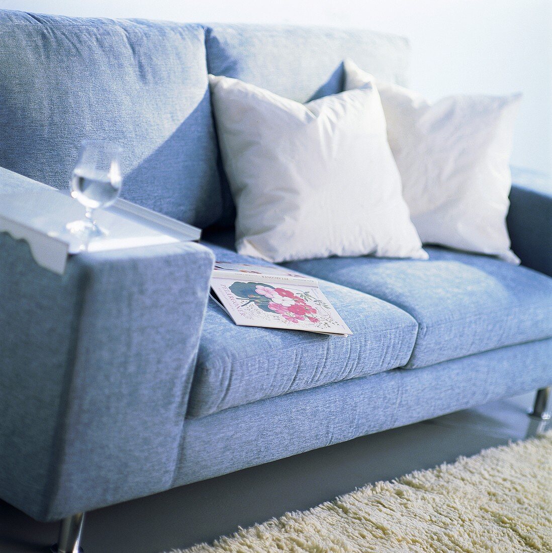 Blaue Couch mit weissen Kissen, Buch und einem Glas Wasser auf der Armlehne