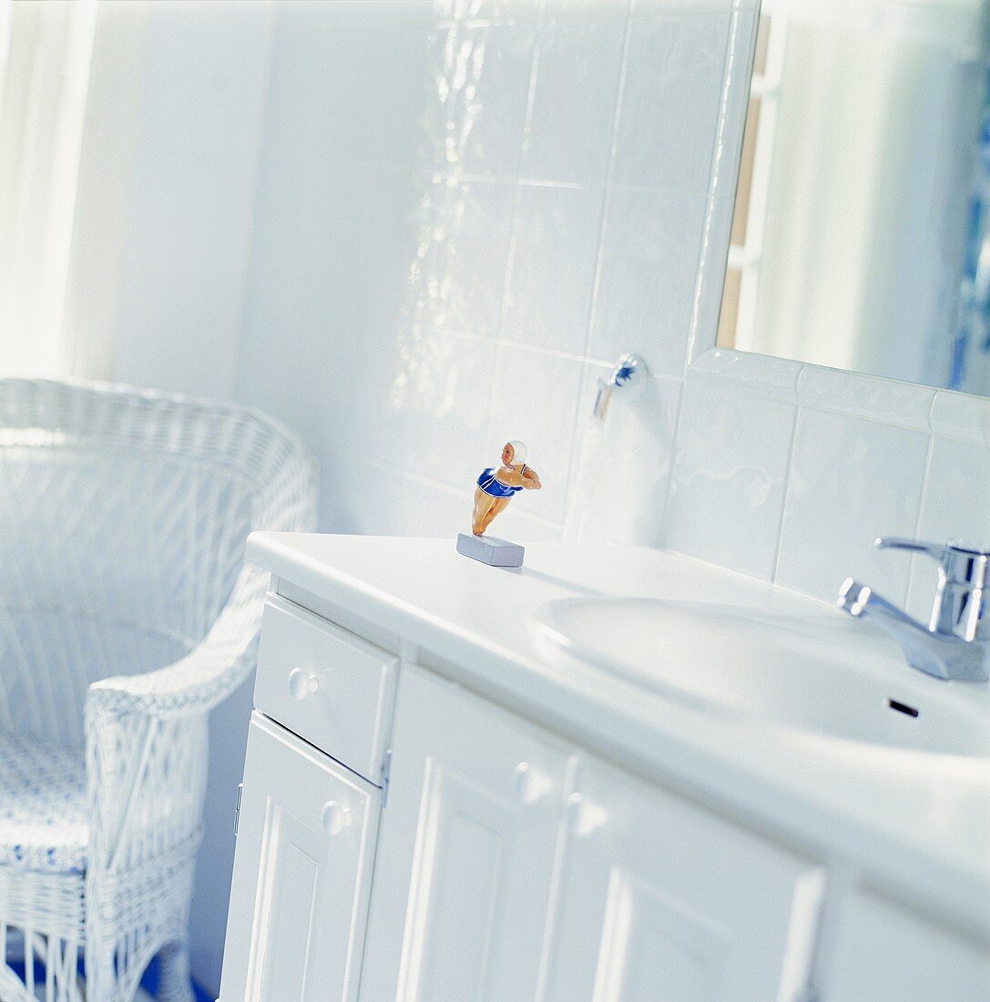 Waschbecken in weiß gefliestem Badezimmer mit weißem Rattanstuhl in der Ecke