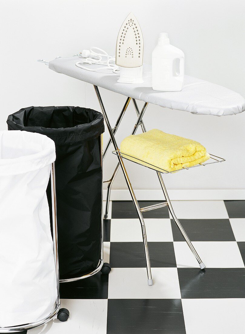 Wäschesäcke in Schwarz und Weiß, Bügelbrett und Bügeleisen in Raum mit Fussboden im Schachbrettmuster