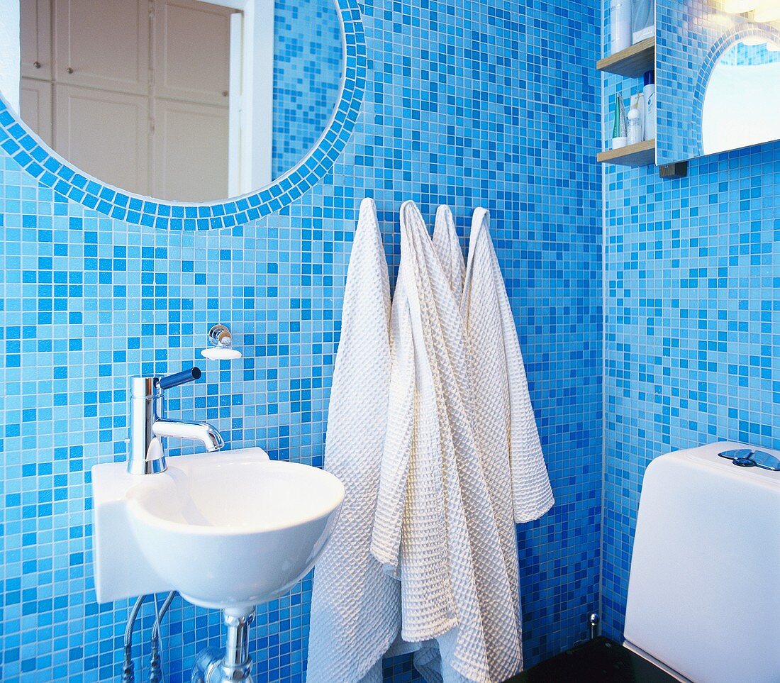 Badezimmer mit blauen Mosaikfliesen und einem eingelegten, ovalen Spiegel