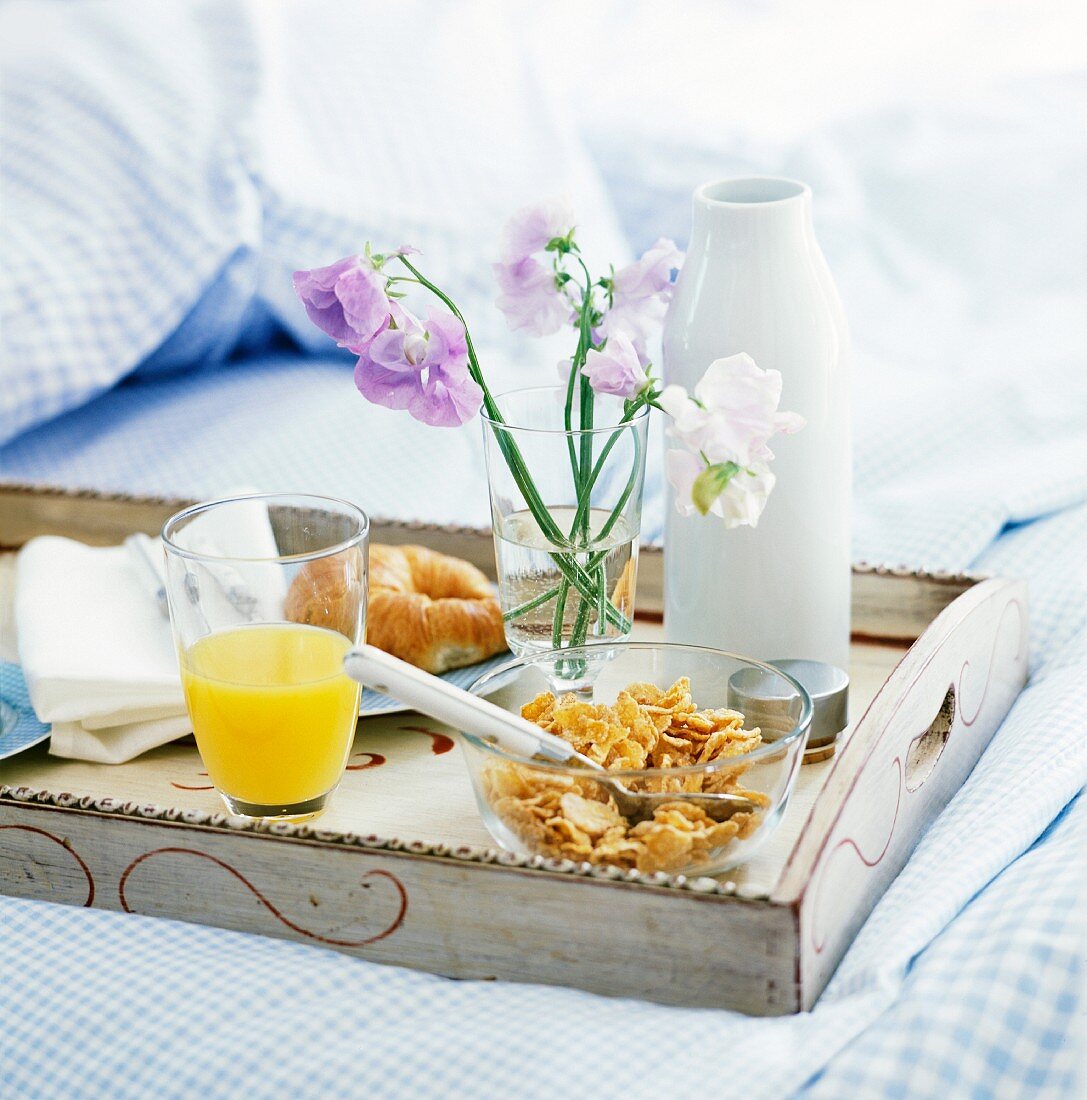 Frühstückstablett mit Croissant, Cornflakes & Orangensaft auf Bett
