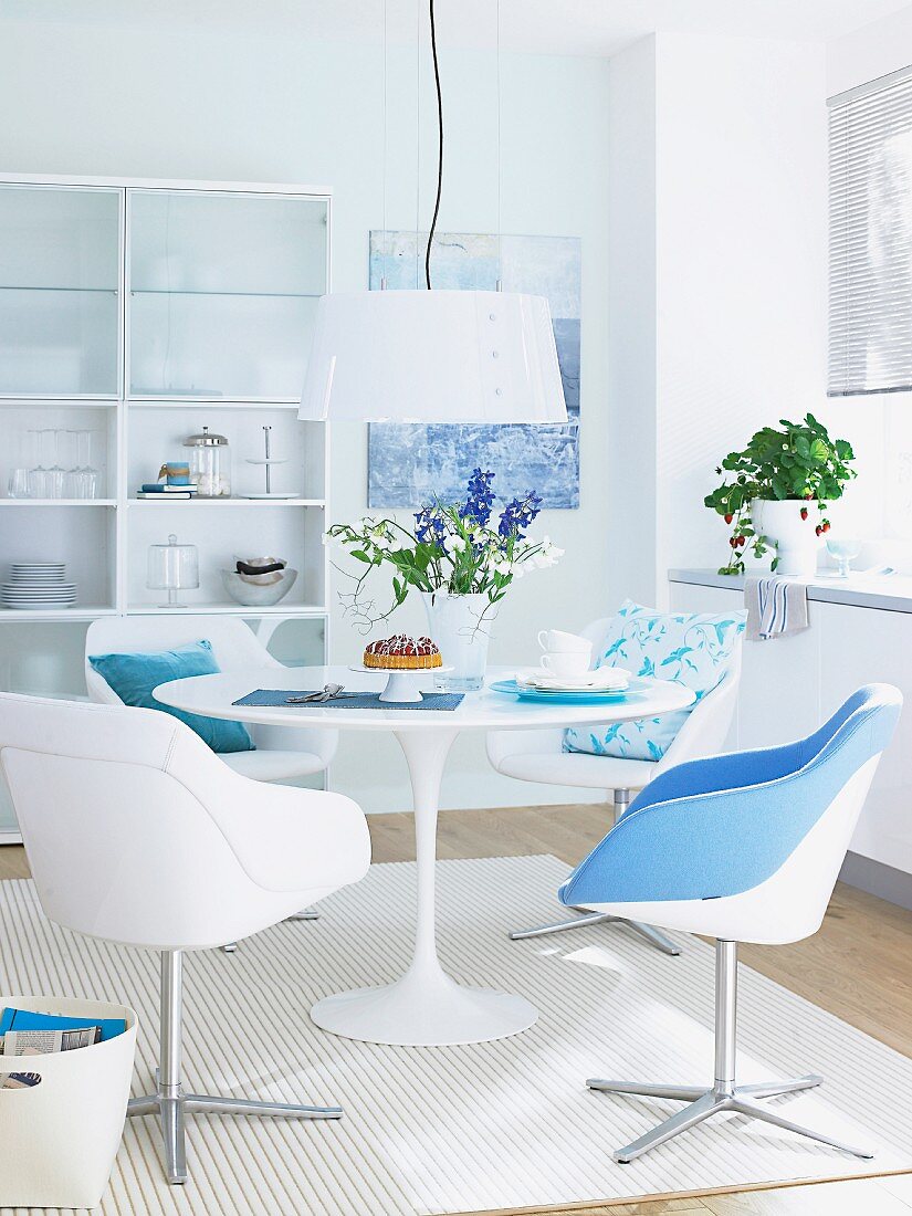 A dining area in white with a round table, bucket chairs and touches of blue