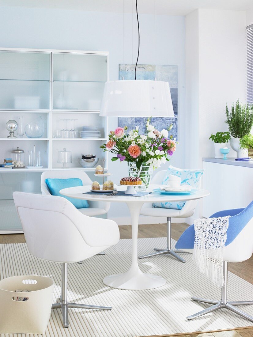 A dining room in white with a round table, bucket chairs and touches of blue