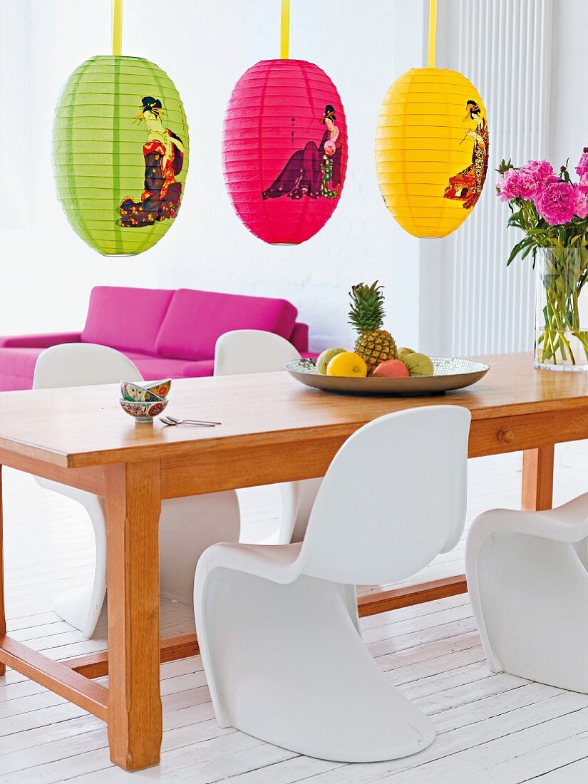 Länglicher Esstisch aus Holz mit weissen Pantonstühlen & bunten Papierlampen mit asiatischem Design