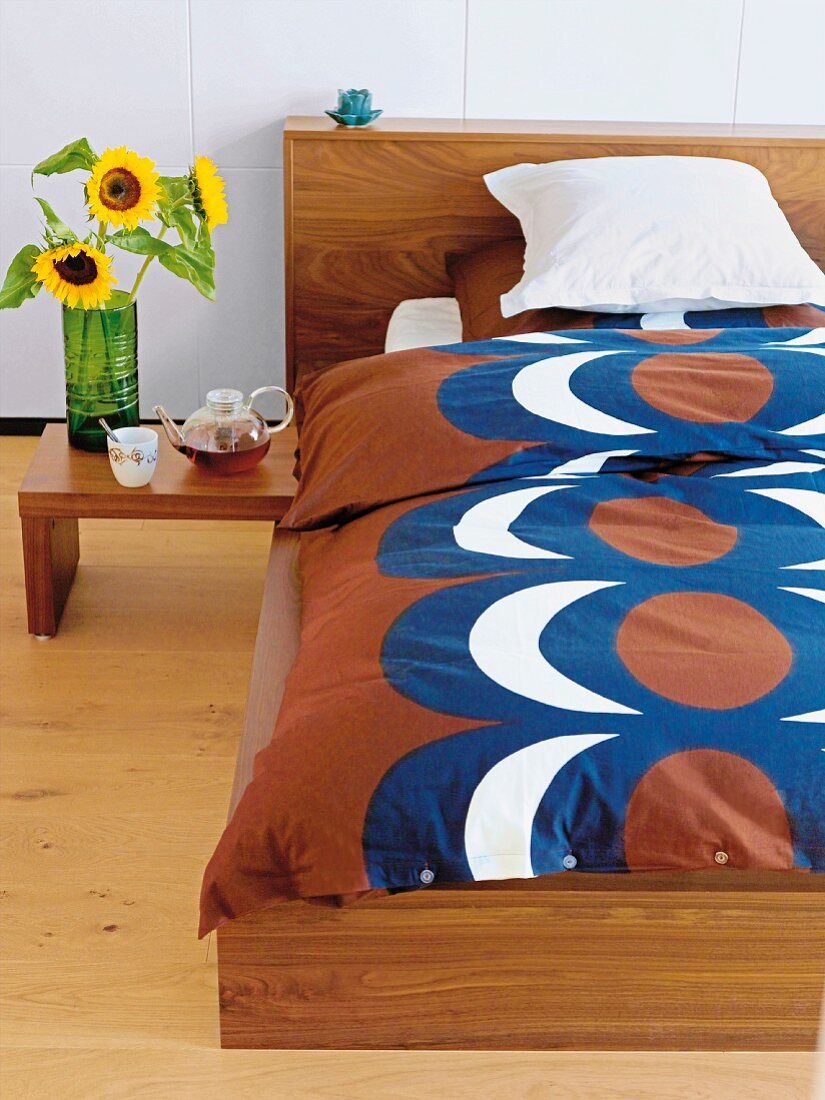 Retro Bettwäsche auf Bett mit Holzgestell, neben angehängtem Beistelltisch, Sonnenblumen in Glasvase