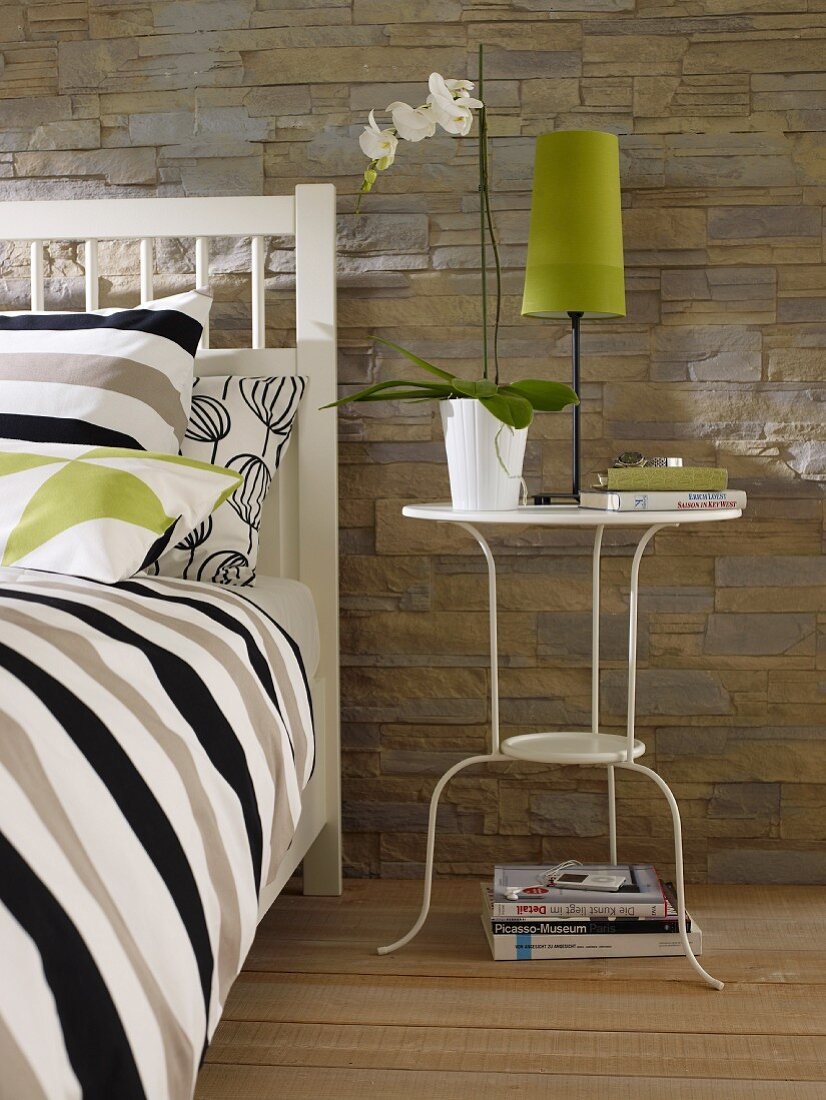 White-painted, metal side table next to bed in bedroom with stone-effect wallpaper