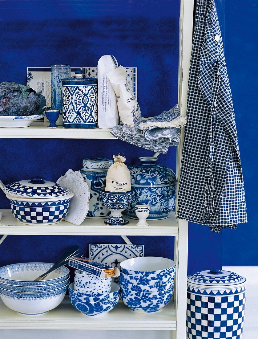 Weisses Holzregal mit Geschirr in Weiß und Blau in ländlichem Stil vor blau getönter Wand