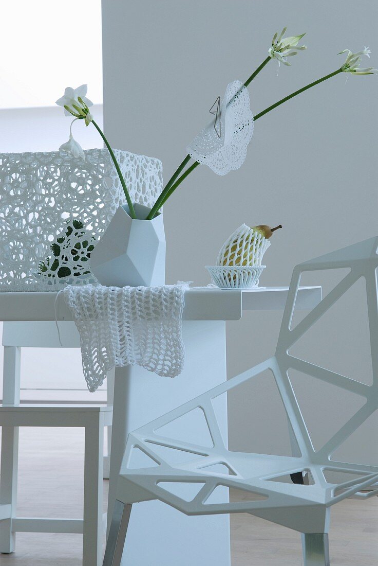 Esstisch in Weiß mit extravagantem Stuhl sowie Blumenvase und Häkelspitze als Tischdeko