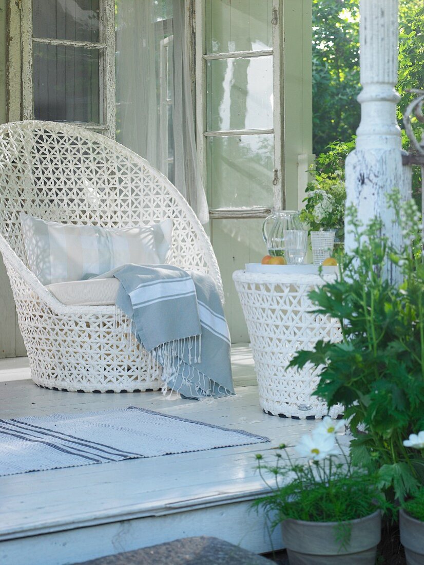 An elegant white wicker chair with a matching table on a summery veranda