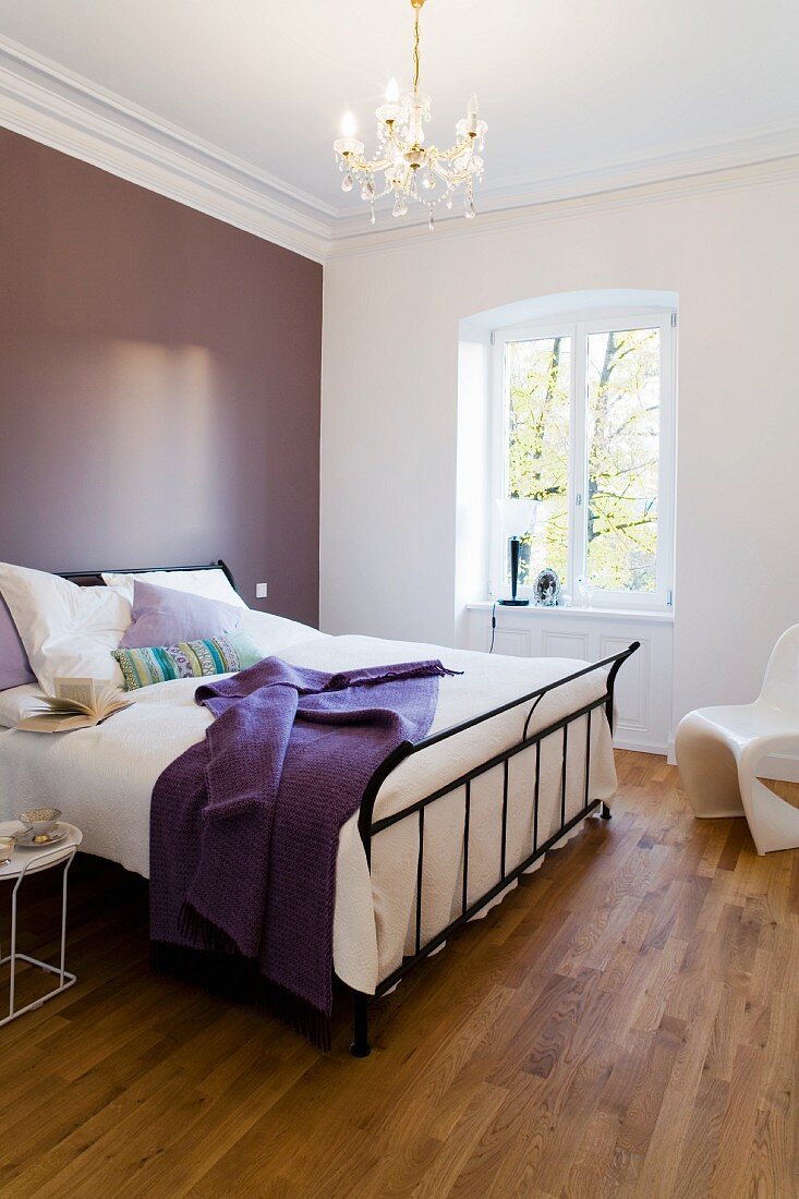 A metal bed against a purple wall in a bedroom in an apartment in a period building