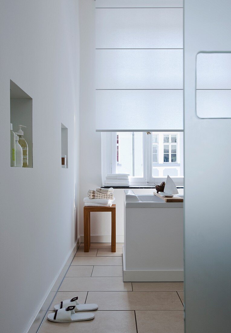 Bad in Weiß mit Fenster, freistehender Badewanne, Fliesenbode & Wandnischen als Stauraum