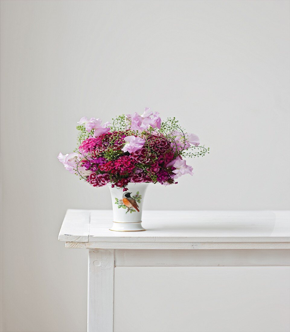 Vase mit Strauss aus Bartnelken, Wicken und Hirtentäschelkraut auf weißem Tisch