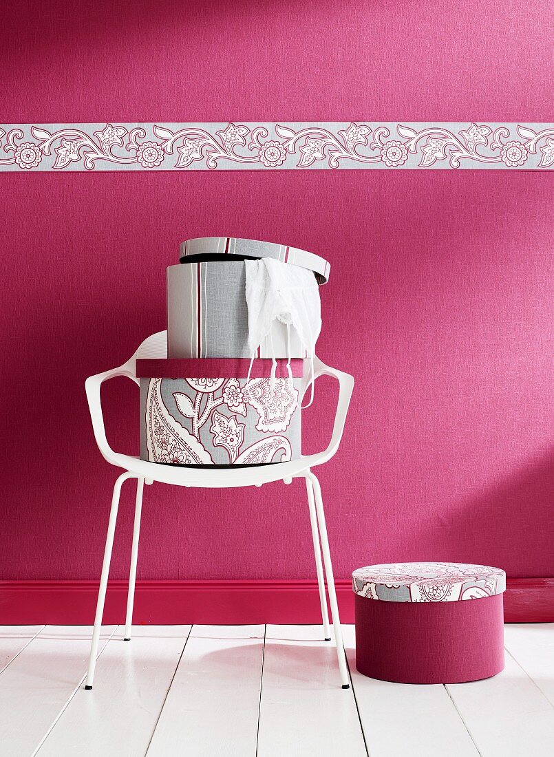 Hatboxes on white chair against deep pink wall