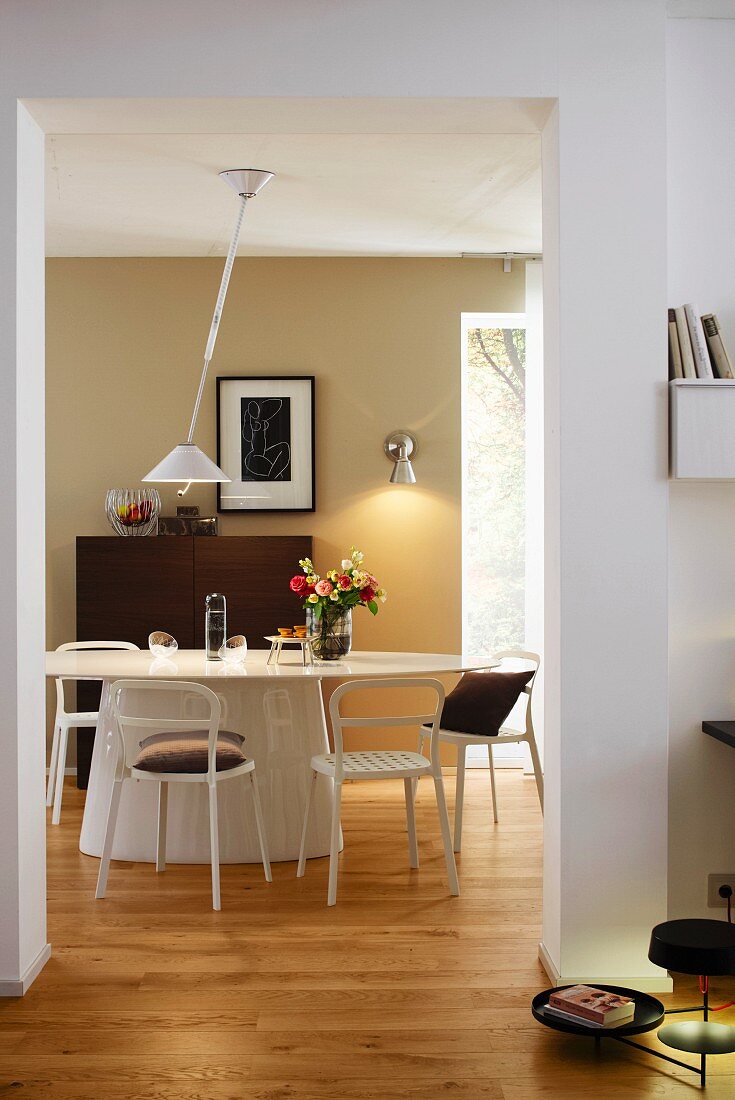 A view into a dining room with an oval table, chairs and a modern pendant lamp