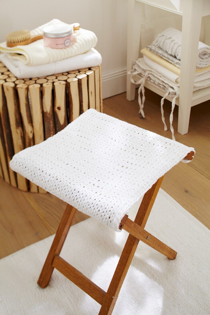 A folding stool with a white knitted seat