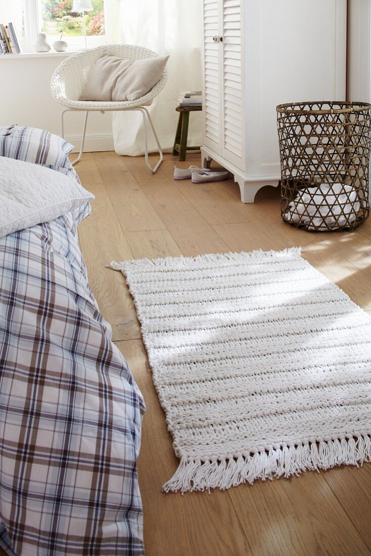 A white knitted rug on wooden floor boards in a bedroom