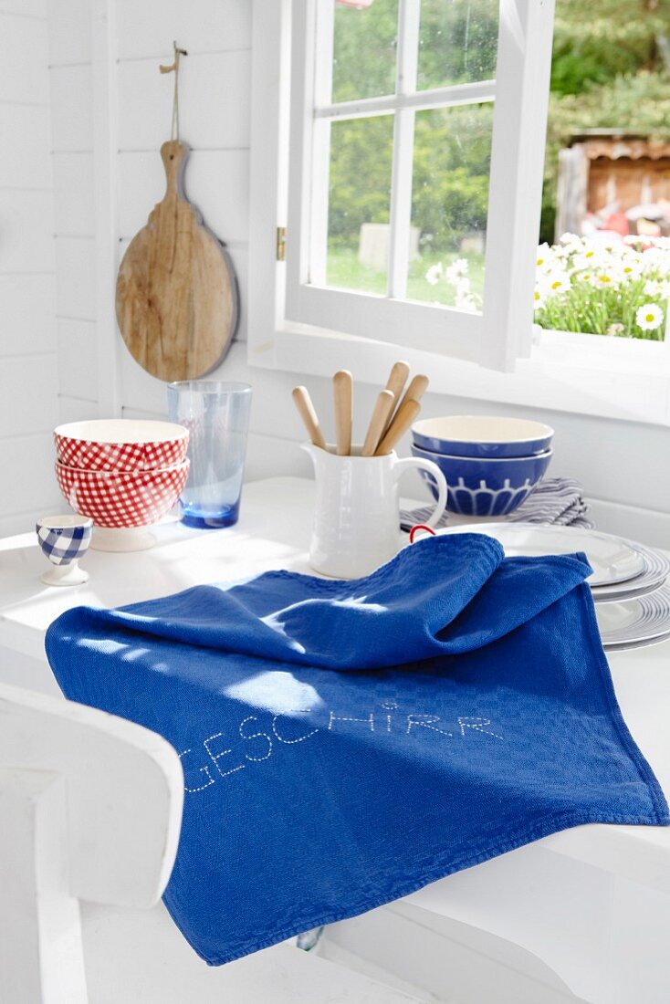 Blaues besticktes Geschirrtuch auf Küchentisch vor Fenster