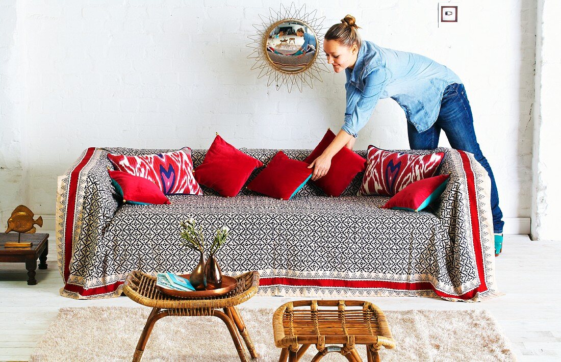 Frau arrangiert Dekokissen auf Sofa mit bunter Decke