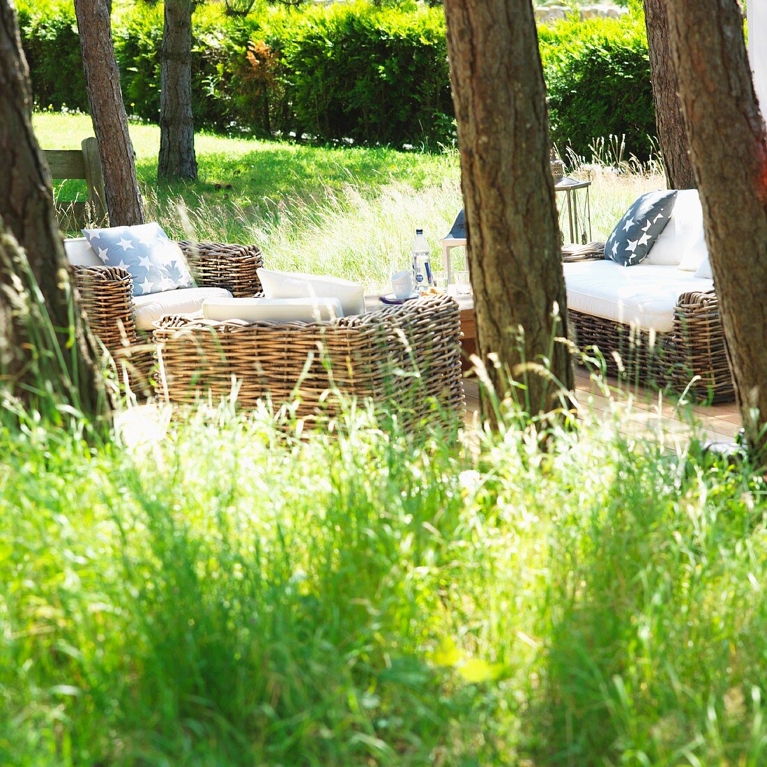 Idyllischer Sitzplatz unter Bäumen mit Korbmöbeln in sommerlichem Garten